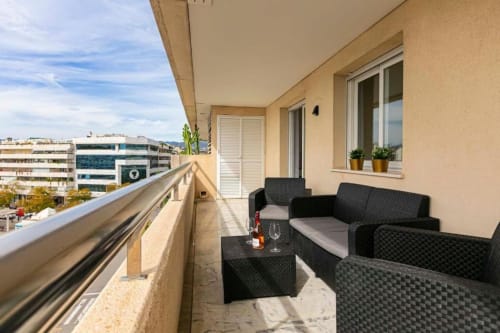 Sunny balcony at Marbella Marina Banús apartment with black seating, city views, and potted plants