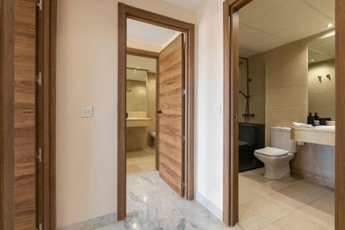 Modern bathroom hallway in Marbella apartment with wood doors, marble flooring, and shower area visible