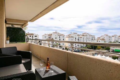 Balcony view of white-washed buildings in Marbella, Puerto Banús with seating area and wine bottle