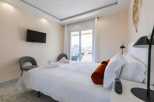 Modern bedroom at Marbella Home Rentals with white bed, city views, TV, and contemporary decor in Puerto Banús apartment
