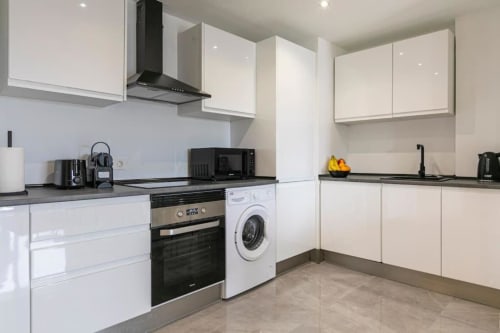 Modern white kitchen with black countertops, stainless steel appliances, and washing machine at Marbella Home Rentals Marina
