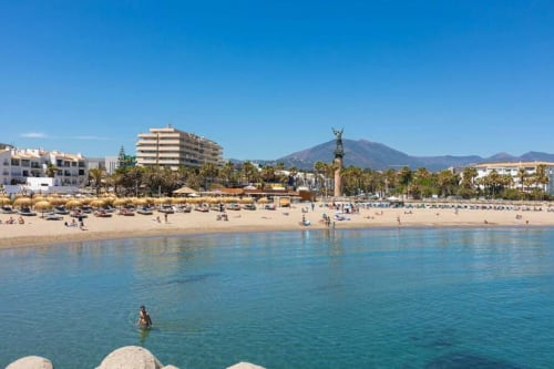 Marbella beach with clear turquoise water, sandy shore, palm trees, and mountain view in background