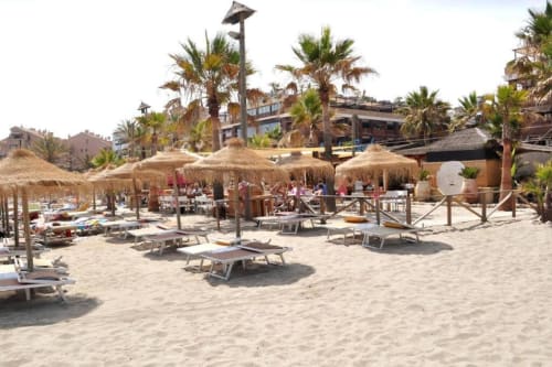 Beach club with thatched umbrellas, loungers, and palm trees at Marbella vacation rental