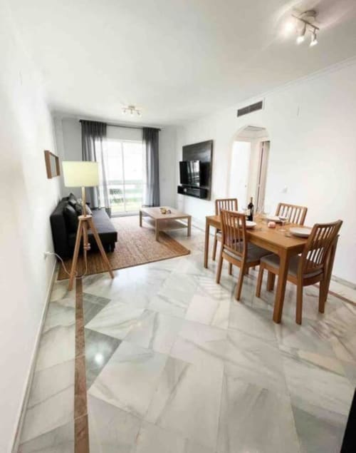 Modern Marbella apartment living and dining area with marble flooring, wooden furniture, and balcony view