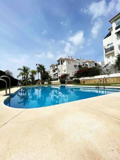 Sparkling oval pool with sunlit terrace overlooking white apartment buildings in Marbella's Nueva Andalucía