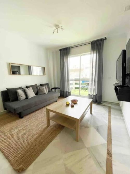 Modern living room with gray sofa, wooden coffee table, and garden view balcony in Marbella apartment
