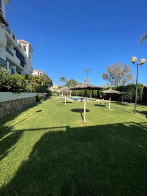 Lush garden view at Lorcrimar I apartment in Marbella with manicured lawn, umbrellas, and modern building amenities under