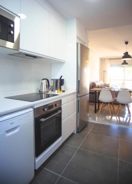 Modern white kitchen with stainless steel appliances and dining area in Marbella apartment rental
