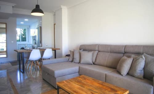 Modern living room in Marbella apartment with beige sofa, wooden coffee table, and open kitchen area with pendant lighting