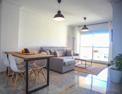 Modern Marbella apartment living room with gray sofa, dining table, pendant lights, and terrace view in Nueva Andalucía