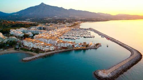 Aerial view of Marbella beachfront with Puerto Banús marina, white apartments, turquoise Mediterranean waters, and mountain