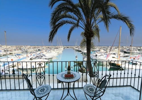 Balcony view of Puerto Banús marina with sailboats, palm tree, and dining table at Marbella apartment
