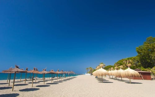 Pristine sandy beach in Marbella with thatched umbrellas and clear blue Mediterranean sea, Puerto Banús coastal view