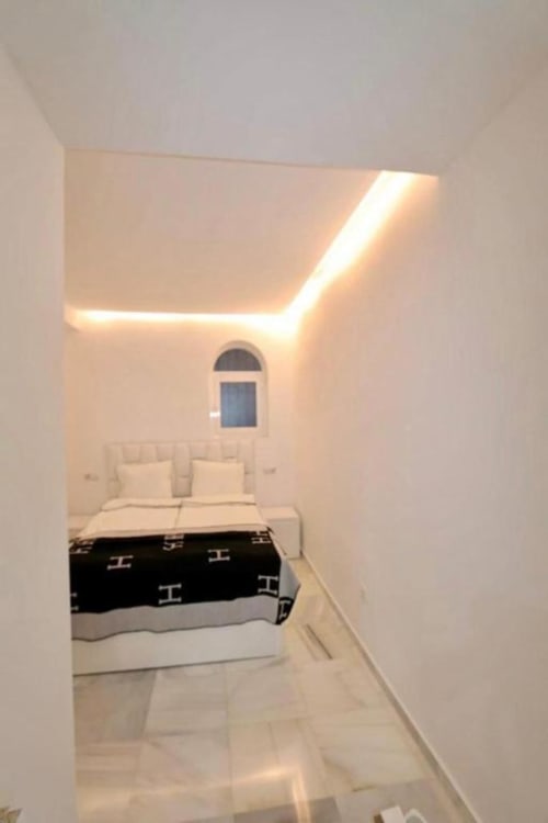 Modern bedroom with ambient ceiling lighting, arched window, and black and white bedding in Marbella apartment