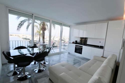 Luxury Marbella apartment with sea view, modern white kitchen, black accent furniture, and terrace overlooking Puerto Banús