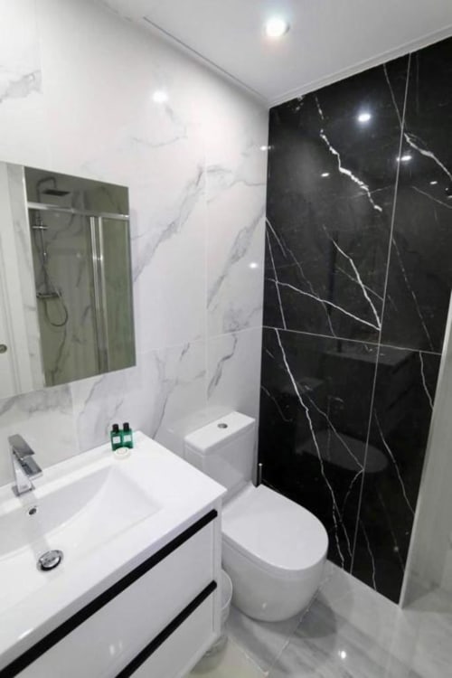 Modern bathroom with white sink vanity, black marble tile shower wall, and mirror in Marbella apartment