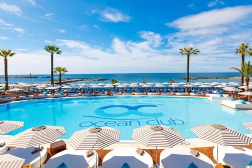 Oceanclub pool with striped umbrellas overlooking Mediterranean Sea in Puerto Banús, Marbella