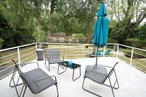 Terrasse moderne au bord de la rivière à Accolade avec chaises longues, parasol bleu et vue sur la vallée verdoyante de Châteaudun