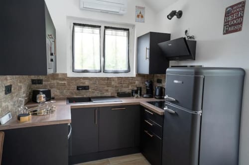 Cuisine cottage moderne à Accolade Châteaudun avec armoires noires, électroménagers inox et dosseret en brique