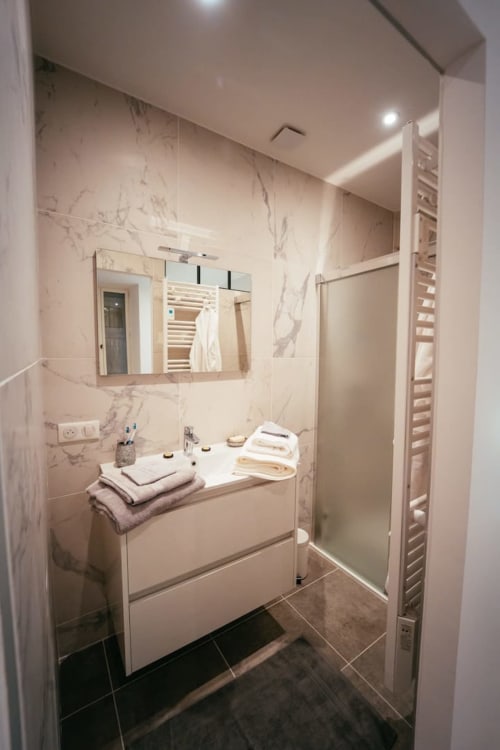 Salle de bains moderne du cottage Accolade à Châteaudun avec murs en marbre, vasque blanche, sèche-serviettes chauffant et douche à l'italienne
