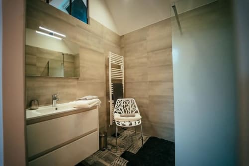 Salle de bain moderne du gîte Accolade à Châteaudun avec vasque, miroir, radiateur sèche-serviettes et chaise contemporaine