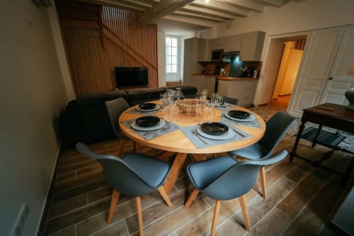 Coin repas contemporain du cottage Accolade à Châteaudun avec table ronde en bois, chaises bleues et cuisine ouverte