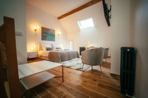 Chambre de la suite Accolade au Château-Dun avec poutres apparentes, lit queen-size, coin salon et vue sur la ville