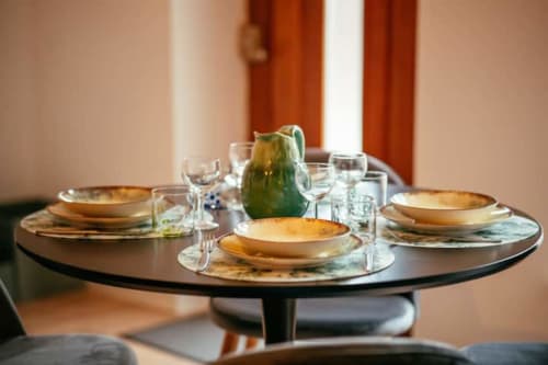 Table de salle à manger élégante et ronde à l'appartement Accolade à Châteaudun, dressée pour trois avec assiettes à liseré doré et verres en cristal