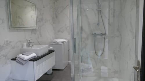 Salle de bain moderne de l'appartement Accolade à Châteaudun avec carrelage marbre, douche ouverte, vasque et serviettes blanches