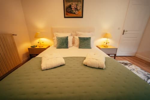 Spacieuse chambre de l'appartement Accolade à Châteaudun avec literie verte, oreillers blancs, lampes de chevet jumelles et ambiance chaleureuse