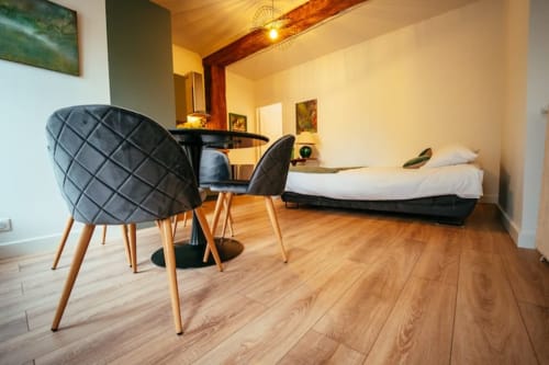 Appartement moderne Accolade à Châteaudun avec chaises matelassées noires, petite table à manger et lit sur sol en bois