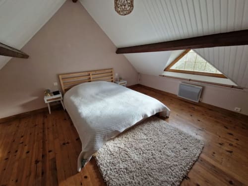 Chambre mansardée lumineuse au gîte Accolade à Châteaudun avec poutres en bois, fenêtre sur le jardin et parquet rustique.