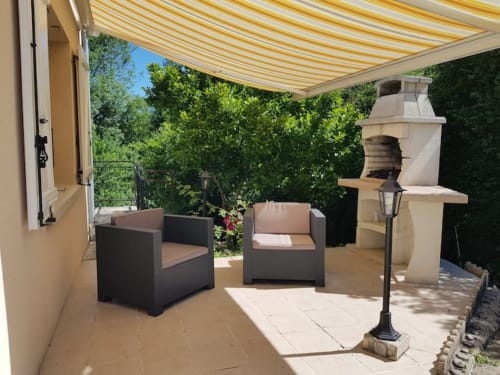 Patio ombragé du gîte Accolade à Châteaudun avec salon, store rayé et verdure luxuriante