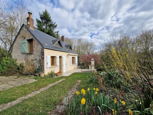 Cottage Accolade à Châteaudun avec fleurs jaunes de printemps, vue sur le jardin, façade pierre et crème, toit d'ardoise