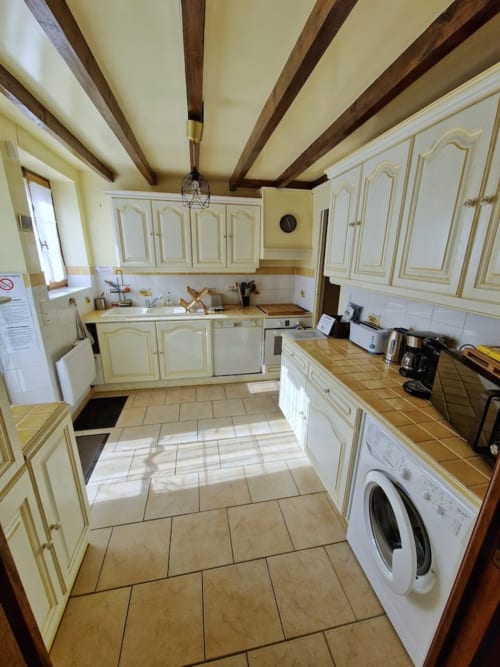 Cuisine spacieuse d'Accolade Châteaudun avec armoires crème, poutres apparentes, carrelage et vue sur jardin.