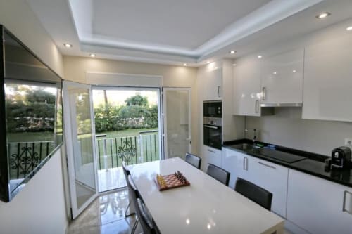 Cocina y comedor modernos en apartamento frente a playa en Marbella, con balcón con vista al jardín y muebles blancos