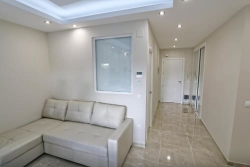 Sala de estar moderna con sofá cama crema, entrada a cocina y pasillo en apartamento frente al mar en Marbella
