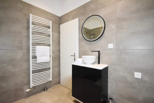 Salle de bains moderne à Illkirch-Graffenstaden avec vasque noire, miroir rond, radiateur sèche-serviettes blanc et carrelage neutre