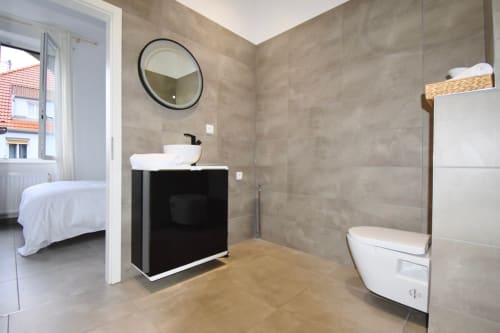 Salle de bains moderne avec meuble-lavabo noir, miroir rond et toilettes dans un appartement à Illkirch-Graffenstaden