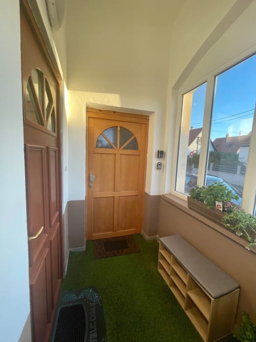 Entrée moderne avec porte en bois, moquette verte, banc et baie vitrée panoramique dans l'appartement d'Illkirch-Graffenstaden