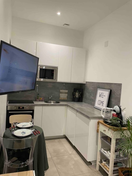 Cuisine moderne blanche avec plan de travail gris, table à manger, télévision et pancarte bienvenue dans l'appartement d'Illkirch-Graffenstaden