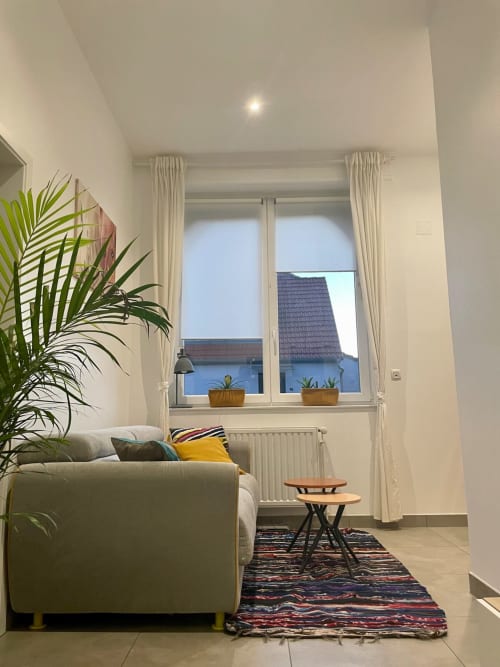 Salon moderne à Illkirch-Graffenstaden avec vue sur la ville, canapé crème, plantes et grandes fenêtres lumineuses
