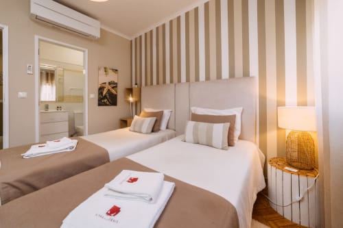 Quarto twin do hotel Casa da Praia em Zambujeira do Mar com cabeceira listrada, casa de banho privativa e iluminação acolhedora