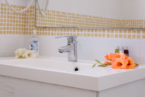 Elegant bathroom sink at Casa da Praia with white counter, chrome faucet, fresh flowers, and yellow tiled backsplash