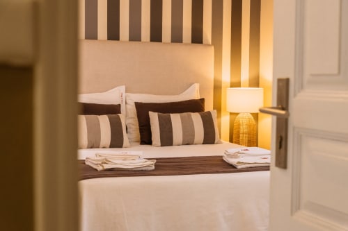 Double bed at Casa da Praia hotel in Zambujeira do Mar with striped pillows, warm lighting, and folded towels