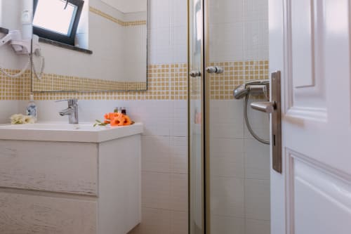 Modern bathroom with white and golden tile work, sink, shower with glass enclosure, and decorative flowers at Casa da Praia,