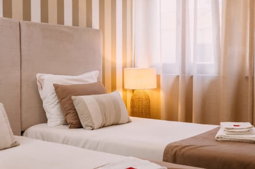 Bright double room at Casa da Praia with twin beds, beige headboard, striped curtains, warm bedside lamp, and beach house