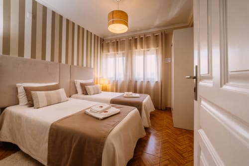 Spacious double bedroom at Casa da Praia with twin beds, striped headboard, wooden floors, and ocean views in Zambujeira do