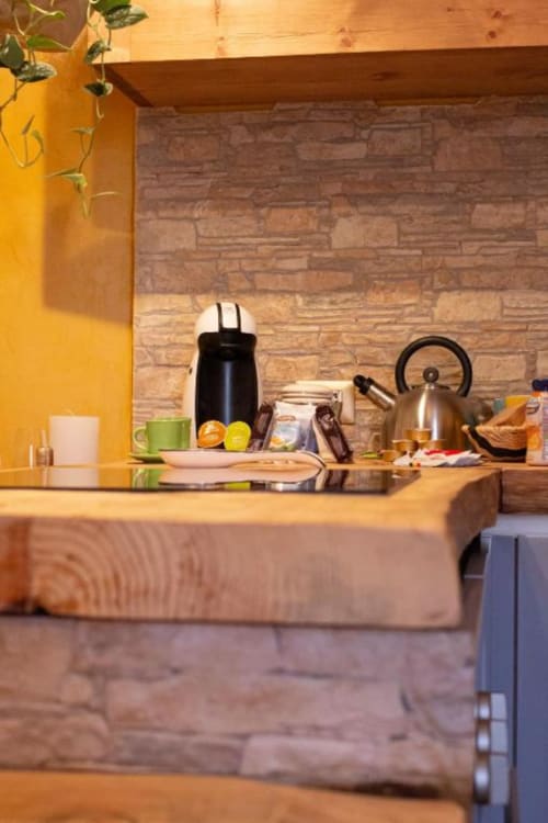 Cucina moderna dell'appartamento Dimore Verona con parete accent gialla, bollitore in acciaio inox e rivestimento in laterizio.