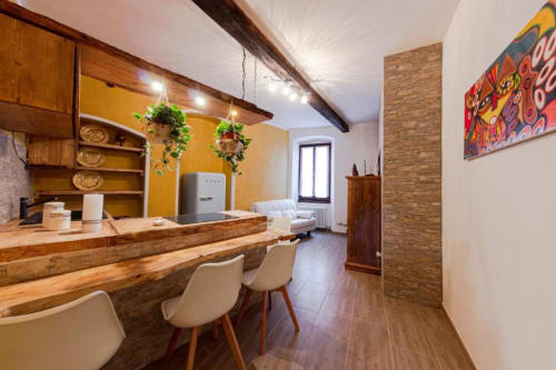 Cucina e soggiorno dell'appartamento Dimore Verona con travi in legno rustico, parete accent gialla e arredi moderni